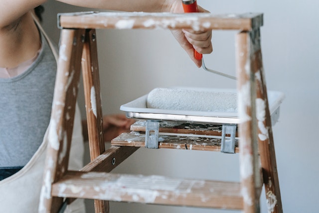 someone rolling a paint roller in a tray on a a ladder